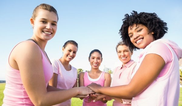 Women wearing pink for breast cancer and putting hands together in parkland