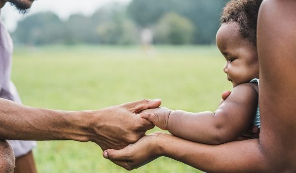 Happy african family holdings hands together outdoor during mother day - Mom, father and daughter having tender moments in nature green park - Love and unity concept