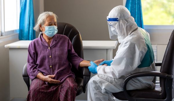 Asian doctor is checking patience's pulse by fingers, medical checking on table. the aging female patient that is at risk for infection corona virus [covid-19].